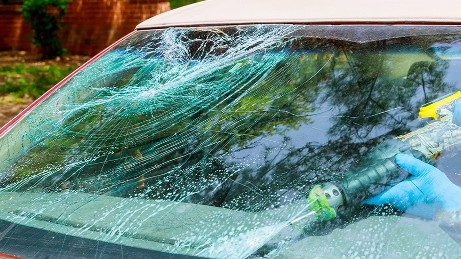 A pressure washer is sprayed onto a heavily shattered car windshield