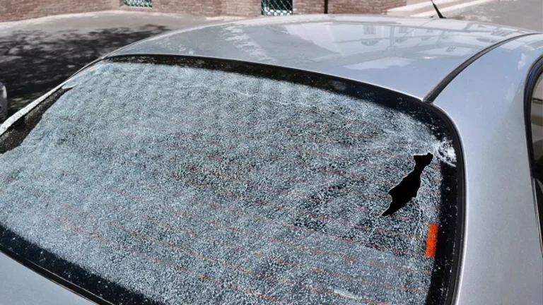 A shattered rear windshield of a silver car with a small hole on the right side