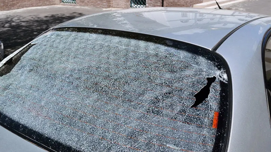 A shattered rear windshield of a silver car with a small hole on the right side